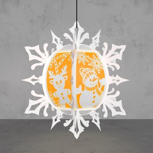 May include: A white paper snowflake Christmas ornament with an orange interior. The ornament features a reindeer and snowman design. The reindeer has candy cane antlers. The snowman wears a hat and scarf. The ornament hangs from a black string.