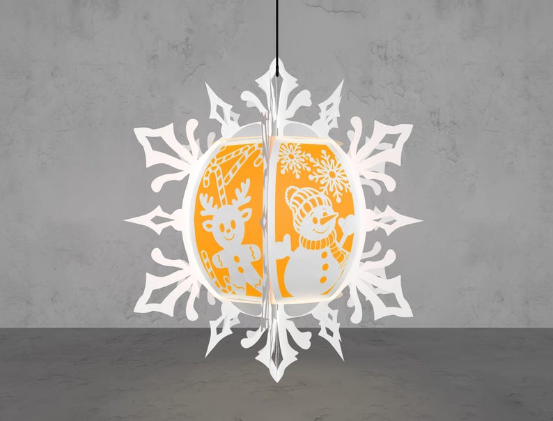 May include: A white paper snowflake Christmas ornament with an orange interior. The ornament features a reindeer and snowman design. The reindeer has candy cane antlers. The snowman wears a hat and scarf. The ornament hangs from a black string.