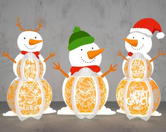 May include: Three snowman ornaments with orange and white paper mache bodies. The snowmen are decorated with Christmas-themed designs and text, including "Ho Ho Ho", "Merry Grinchmas", and "Merry Christmas".