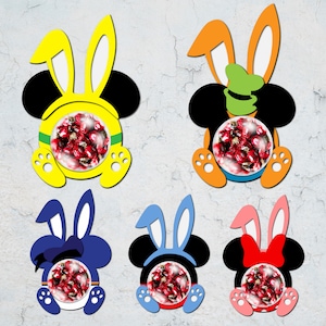 May include: Five Easter bunny-shaped candy holders with Mickey Mouse ears. Each holder is a different colour: yellow, orange, blue, pink, and purple. The holders are filled with red sweets.