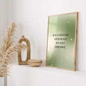 Pode incluir: Uma impress&atilde;o emoldurada com um fundo gradiente verde e branco e o texto "IF IT COSTS YOU YOUR PEACE IT'S TOO EXPENSIVE." A impress&atilde;o est&aacute; em uma moldura de madeira clara. Tigelas de madeira decorativas e um vaso com plantas secas tamb&eacute;m s&atilde;o vis&iacute;veis.