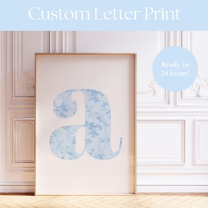 Puede incluir: Una impresión enmarcada con una gran letra "A" en un patrón floral azul claro. La impresión está sobre un fondo crema y enmarcada en madera dorada. El texto "Custom Letter Print" está en la parte superior, y "Ready in 24 hours!" está en un círculo.
