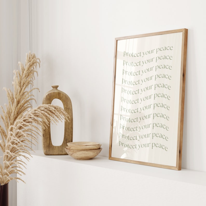 Pode incluir: Uma impress&atilde;o emoldurada com as palavras "Protect your peace" repetidas em uma fonte verde clara. A impress&atilde;o &eacute; exibida com um vaso de madeira, duas tigelas de madeira e grama ornamental seca. A moldura &eacute; feita de madeira clara.