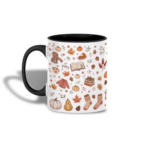 Könnte beinhalten: Ein weißer Keramikbecher mit schwarzem Henkel und schwarzem Innenraum, verziert mit einem wiederkehrenden Muster aus herbstlichen Illustrationen wie Kürbissen, orangefarbenen Blättern, Eicheln, einem Schal, einem Buch, Kuchen und Socken.
