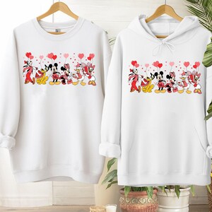 Pu&ograve; includere: Felpa e felpa con cappuccio bianche con una grafica dei personaggi Disney, tra cui Topolino e Minnie, Pippo, Paperino e Paperina, che tengono in mano palloncini a forma di cuore. Il design &egrave; rosso, nero e giallo.