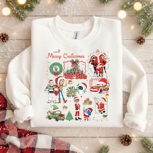 Könnte beinhalten: Weißes Sweatshirt mit einem farbenfrohen Weihnachtsmotiv. Das Design zeigt Zeichentrickfiguren, ein Schloss und den Schriftzug "Merry Christmas". Festliche und fröhliche Kleidung für die Weihnachtszeit.