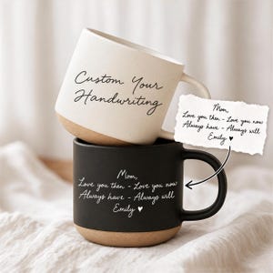 Könnte beinhalten: Ein Stapel aus zwei Keramikbechern. Der obere Becher ist cremefarben mit dem Text Custom Your Handwriting. Der untere Becher ist mattschwarz mit dem Text Mom, Love you then - Love you now Always have - Always will Emily und einem Herzsymbol.