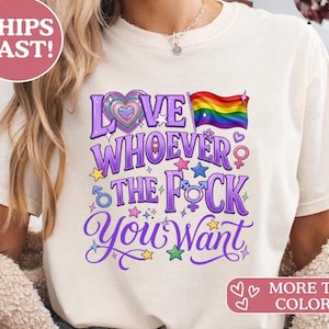 Könnte beinhalten: Cremefarbenes T-Shirt mit einem lila Aufdruck mit der Aufschrift "LOVE WHOEVER THE F*CK YOU WANT" mit einer Regenbogenflagge und anderen Symbolen. Das Shirt hat eine lockere Passform und kurze Ärmel.