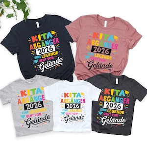 Può includere: Cinque magliette di diversi colori con la scritta in tedesco "KITA ABGÄNGER 2026 EINE LEGENDE GEHT VOM Gelände". Le magliette sono blu navy, rosa, grigio, bianca e antracite, con un design colorato.