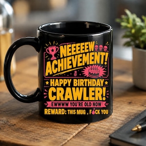 Könnte beinhalten: Ein schwarzer Keramikbecher mit gelbem und pinkfarbenem Grafiktext, der NEEEEW ACHIEVEMENT! HAPPY BIRTHDAY CRAWLER! EWWWW YOU'RE OLD NOW REWARD: THIS MUG, FOCK YOU liest. Das Design enthält einen Pokal, Totenköpfe, eine Geburtstagstorte und ein Bombensymbol.