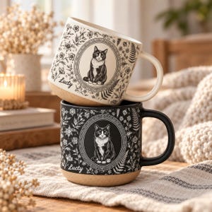 Op de afbeelding: Twee keramische mokken verticaal gestapeld, één crème en één zwart. Elke mok heeft een centraal ovaal kader met een zwart-witte illustratie van een kat, omringd door botanische patronen en de naam Lucty in cursief schrift.