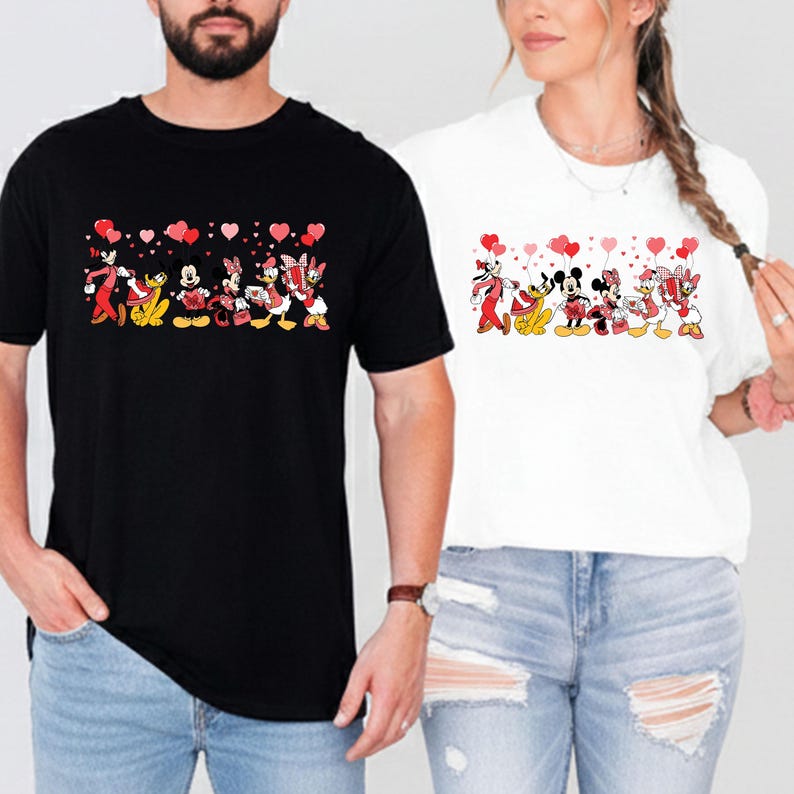 Pu&ograve; includere: T-shirt bianche e nere con un design a cartoni animati di personaggi Disney che tengono in mano palloncini a forma di cuore. I personaggi includono Topolino, Minnie, Paperino, Paperina e Pippo. Le magliette sono indossate da due persone.