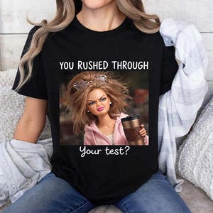 Könnte beinhalten: Schwarzes T-Shirt mit dem Text "YOU RUSHED THROUGH Your test?" über einem Puppenbild. Die Puppe hat eine Sonnenbrille auf dem Kopf und hält einen Kaffeebecher. Die Puppe trägt einen rosa Kapuzenpullover.