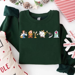 May include: Dark green sweatshirt featuring a line of cartoon characters from Beauty and the Beast. The characters include Belle, Cogsworth, Lumiere, Mrs. Potts, Chip, and the enchanted rose. The sweatshirt has a crew neck and long sleeves.