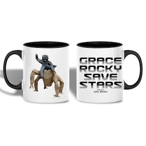 Könnte beinhalten: Weißer Keramikbecher mit schwarzem Innenraum und Griff. Eine Seite zeigt eine graue Figur, die auf einem beigefarbenen, geometrischen Wesen reitet. Die andere Seite zeigt den Text "GRACE ROCKY SAVE STARS" in fetter, schwarzer Schrift, darunter "HAIL MARY".