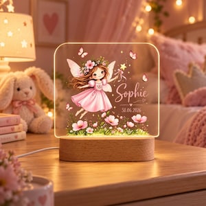 May include: A rectangular acrylic night light with a wooden base featuring a printed illustration of a fairy with brown hair in a pink dress, surrounded by flowers and butterflies. The text reads Sophie and the date 30.06.2026 in white script.