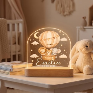 Könnte beinhalten: Ein bogenförmiges Acryl-Nachtlicht mit Holzsockel, bedruckt mit einem Heißluftballon, in dem ein Löwe, ein Tiger und ein Elefant sitzen. Das Design zeigt Sterne, Wolken, eine Mondsichel und den Schriftzug Emilia 08-08-2026.