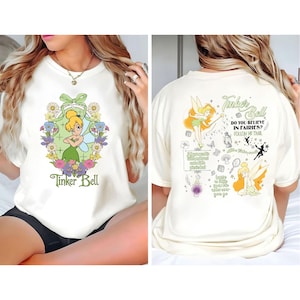Könnte beinhalten: Cremefarbenes T-Shirt mit Tinker Bell, floralen Akzenten und dem Text "Tinker Bell" auf der Vorderseite. Die Rückseite des Shirts zeigt eine Tinker Bell-Grafik und den Text "Do you believe in fairies? Follow mi trail."