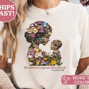 Könnte beinhalten: Cremefarbenes T-Shirt mit einem floralen Design einer Mutter und eines Kindes. Das Design besteht aus verschiedenen bunten Blumen. Der Text "Her children rise up and call her blessed. Sprüche 31:28" ist darunter gedruckt.
