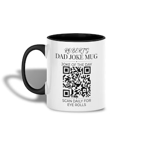 Könnte beinhalten: Ein weißer Keramikbecher mit schwarzem Henkel und Rand. Die Vorderseite zeigt den Text ROBERTS DAD JOKE MUG, JOKE OF THE DAY und SCAN DAILY FOR EYE ROLLS, zentriert um einen schwarz-weißen QR-Code, der für tägliche Witze gescannt werden kann.