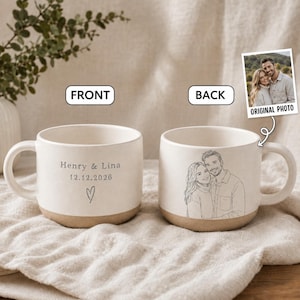 Könnte beinhalten: Zwei cremefarbene Keramiktassen mit beigem Boden. Die vordere Tasse zeigt den Text Henry & Lina, das Datum 12.12.2026 und ein kleines Herz. Die hintere Tasse zeigt eine Strichzeichnung eines Paares, basierend auf dem Originalfoto.