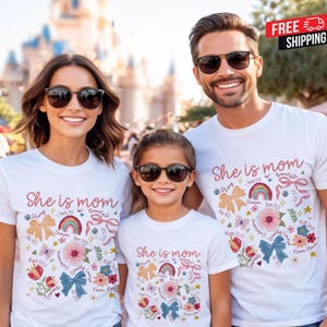 Könnte beinhalten: Drei Personen tragen weiße T-Shirts mit dem Text "She is mom" in rosa Schrift. Die Shirts zeigen Blumen- und Schleifengrafiken, einen Regenbogen und inspirierende Sätze. Alle drei tragen Sonnenbrillen.