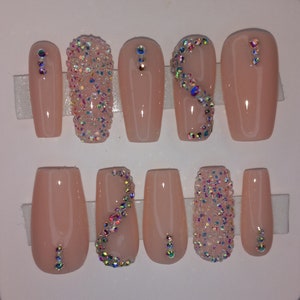 May include: Set of ten nude-colored coffin-shaped press-on nails with various rhinestone designs. Some nails have a single row of rhinestones, while others have a scattered design or a swirl pattern.
