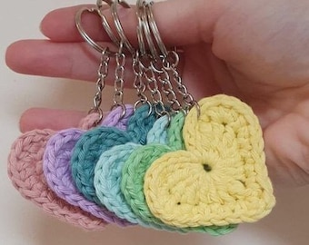 May include: A set of six crocheted heart-shaped keychains in pastel colors, including pink, lavender, teal, green, and yellow. Each keychain is attached to a silver key ring.