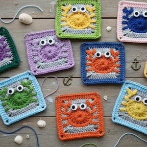 May include: A collection of colorful, square crochet crab appliques with googly eyes. The crabs are in various colors, including green, purple, orange, blue, and yellow, with matching borders. The appliques are arranged on a wooden surface with nautical-themed embellishments.