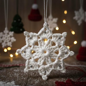 Puede incluir: Primer plano de un adorno navideño de copo de nieve blanco tejido a ganchillo con cuentas plateadas. Otros adornos tejidos a ganchillo incluyen gorros a rayas rojas y blancas, árboles verdes y otros copos de nieve.