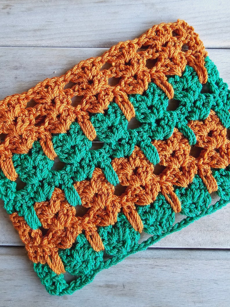 Puede incluir: Un cuadrado tejido a crochet con un patr&oacute;n verde y naranja. El cuadrado est&aacute; hecho con un punto sencillo y tiene un aspecto texturizado.