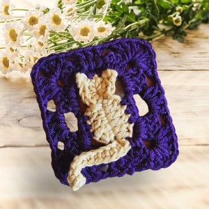 May include: A crocheted square with a purple background and a yellow cat design. The square is made with a single crochet stitch and has a textured look.