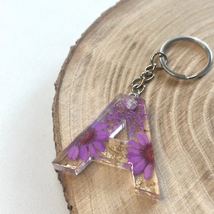 Llavero hecho a mano en resina epoxi en forma de letra | Accesorio y regalo de alta calidad con flores secas de color violeta.