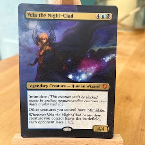 May include: A Magic: The Gathering card featuring Vela the Night-Clad, a legendary human wizard creature with intimidate. The card is blue and black with a purple and white background. The card text reads "Intimidate (This creature can't be blocked except by artifact creatures and/or creatures that share a colour with it.) Other creatures you control have intimidate. Whenever Vela the Night-Clad or another creature you control leaves the battlefield, each opponent loses 1 life. 4/4".