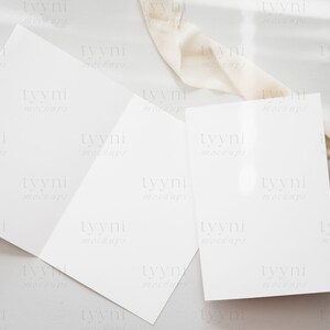 May include: Two blank white cards on a light gray surface with a white fabric draped over the top right corner of the surface.
