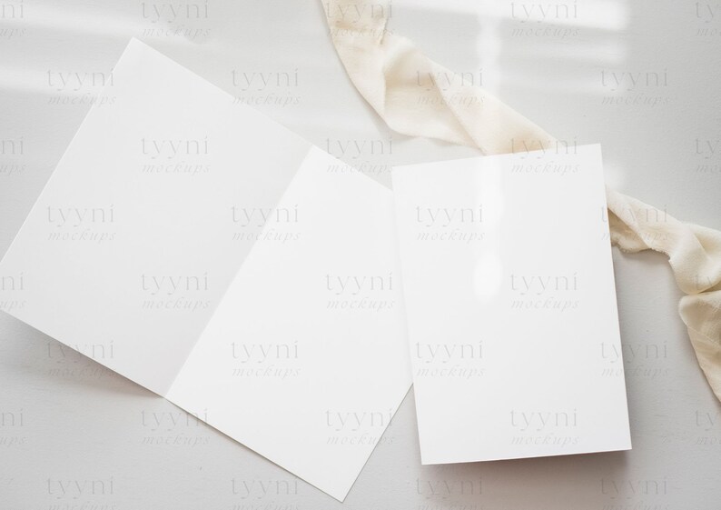 May include: Two blank white cards on a light gray surface with a white fabric draped over the top right corner of the surface.