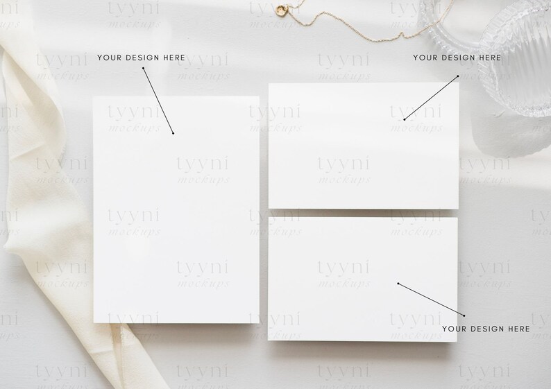 May include: Three blank white cards on a light grey surface with a white fabric draped over the left side of the image. The text "YOUR DESIGN HERE" is written on the image above each card.