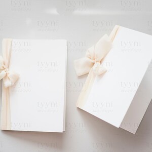 May include: Two blank white cards with a beige ribbon tied around one of the cards. The cards are on a light gray background.