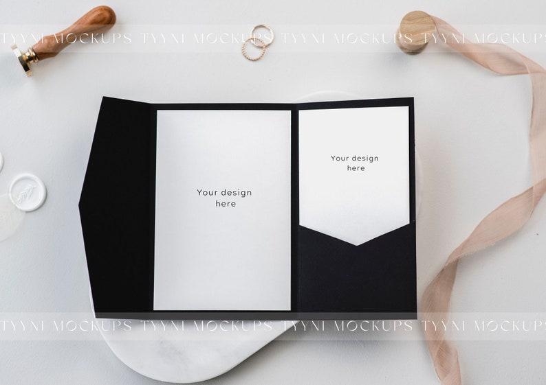 May include: A black invitation card with two white inserts, each with the text "Your design here." The card is on a white surface, with a wax seal, a ribbon, and a gold ring. The overall theme is wedding stationery.