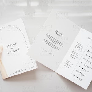 May include: A wedding program booklet with a white cover and a black arch design. The cover reads "Wedding Timeline" and "Aurora and Benjamin". The inside pages include a welcome message and a weekend events timeline.