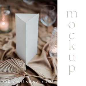 May include: A white triangular table card stands on a draped, tan fabric surface. A dried palm leaf and a wine glass are in the background. The text "mockup" is vertically aligned on the right side of the image. The bottom of the image reads "PSD smart object + JPG".