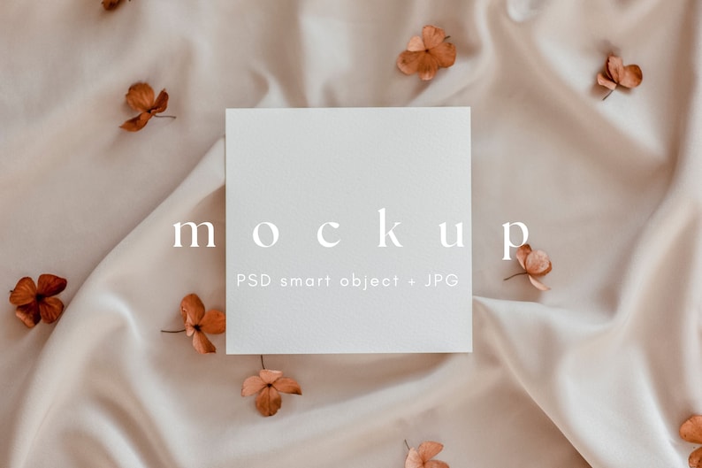 Pu&ograve; includere: Un mockup di una carta bianca con la parola "mockup" in testo bianco e le parole "PSD smart object + JPG" in testo bianco pi&ugrave; piccolo. La carta &egrave; appoggiata su uno sfondo di tessuto beige con fiori marroni secchi sparsi intorno.