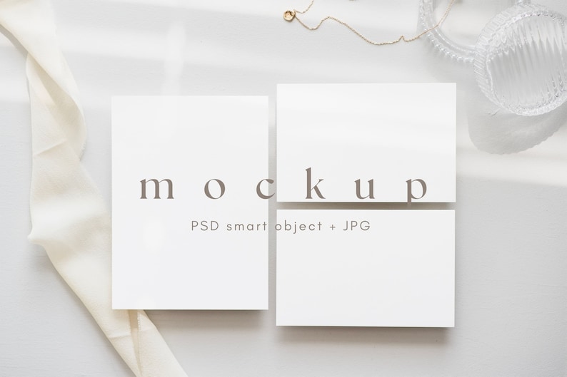 May include: Two white cards with the text "mockup" and "PSD smart object + JPG" on a white surface with a white ribbon and a glass dish.