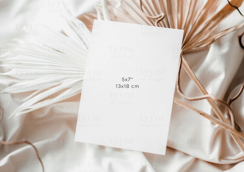 May include: A blank white card with the text "5x7" and "13x18 cm" on a beige fabric background with dried palm leaves.