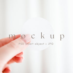 May include: A white round sticker mockup held in a hand. The sticker is blank and ready for your design. PSD smart object + JPG.