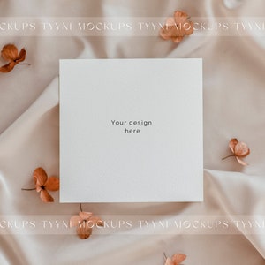 Pu&ograve; includere: Un biglietto bianco con il testo "Your design here" su uno sfondo di raso marrone chiaro con fiori secchi sparsi intorno.