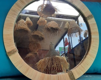 May include: A round mirror with a woven wood frame. The mirror reflects a room with several woven straw lampshades hanging from the ceiling.