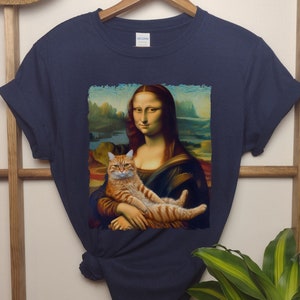May include: A navy blue t-shirt with a graphic print of the Mona Lisa painting, but with a ginger cat sitting on her lap.