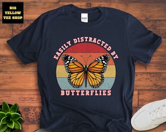 May include: Navy blue t-shirt featuring a vintage-style graphic of a butterfly and the text "Easily Distracted By Butterflies".