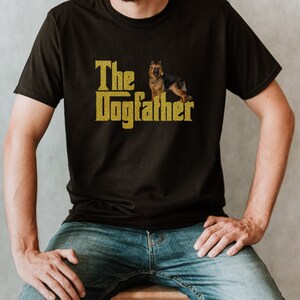 May include: A black t-shirt with a gold glitter design that says "The Dogfather" with a German Shepherd dog standing on its hind legs.